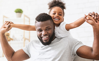 Smiling father and daughter playing together at home, with the daughter joyfully riding on his back.