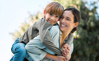 Happy mother and son outdoors, laughing as she gives him a piggyback ride.