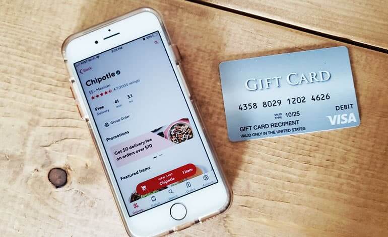 iPhone with DoorDash app open alongside a Visa Gift Card sitting on top of a wooden table