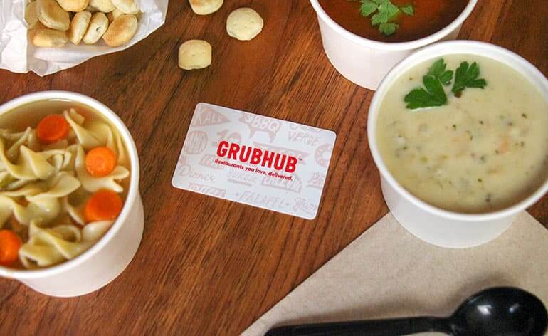 GrubHub gift card lying on table with various cups of soups around it